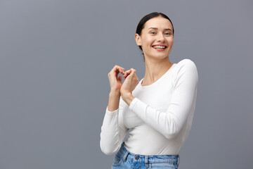 an attractive woman stands on a gray background in a white T-shirt, happily made a heart out of her hands