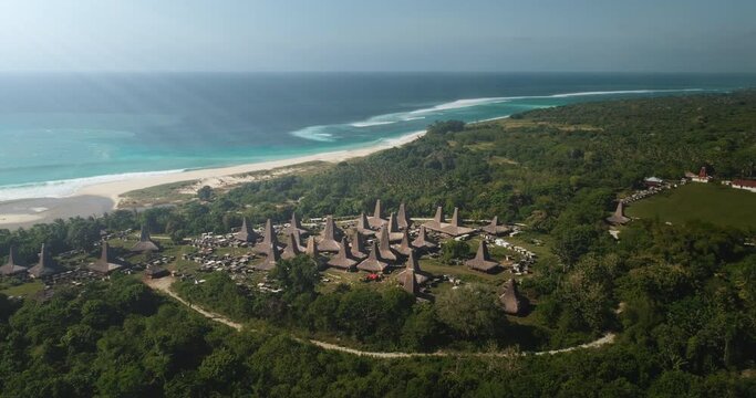 Aerial view of traditional authentic village houses Sumba island. Sandy ocean beach with tropical plants landscape. Unique Indonesia house ornately roofs. Sea sunrise waves. Summer vacation tourism.