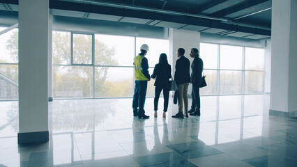 Diverse group of businesspeople standing inside newly constructed industrial building talking...