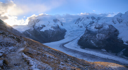 Sunrise over mountain chain above Monte Rosa massif. First rays of the sun over mountains. Male hiker on a trail to the new Monte Rosa hut along the Border Glacier Grenz Gletscher. Vacation in Zermatt