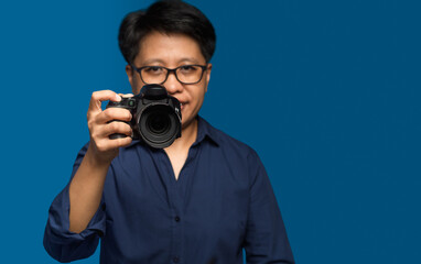 Portrait of a woman with short black hair holding a digital camera while standing on a blue...