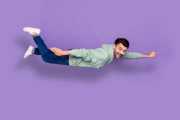Full size photo of handsome young man flying funky funny superman have fun dressed stylish khaki look isolated on purple color background