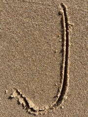 On the beach in the sand is carved the letter J