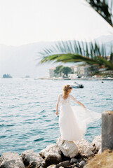 Fototapeta na wymiar Bride in a dress fluttering in the wind stands on the rocks by the sea
