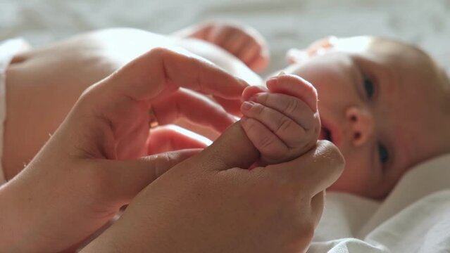 Baby hand in mother hands, on her palm. Happy parents holding their newborn baby tiny fingers, close up. Maternity, family, birth concept. Woman touching hand of infant baby. Mom and her Child.