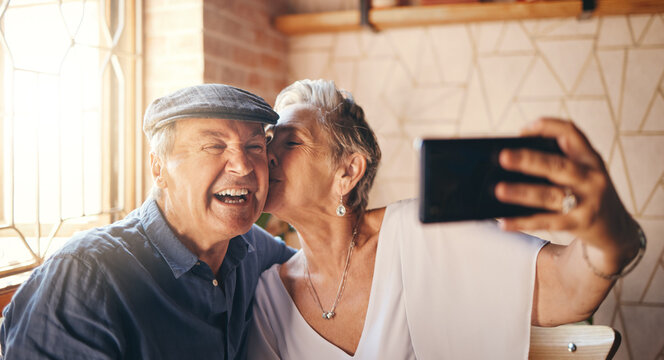 Love, phone and selfie with elderly couple kiss and relax in their home together, laughing and bonding. Photography, retirement and seniors enjoying retired lifestyle and romance in their living room