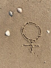 In the sand on the beach is carved the sign for female