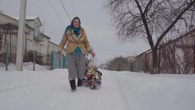 grandmother pulls a child on a sled,a grandmother pulls a sled with her granddaughter through the snow, an older woman with a little girl in winter
