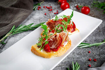 Delicious snacks. Bruschetta with bacon, roasted tomato, red onion rings and arugula. Toasted croutons with dried meat and lettuce