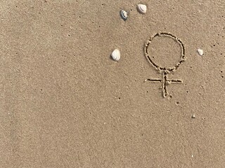 Fototapeta na wymiar In the sand on the beach is carved the sign for female