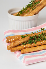 Crispy bread sticks grissini with thyme stems and sesame seeds. Fragment of traditional Italian pastry breadsticks on striped table napkin