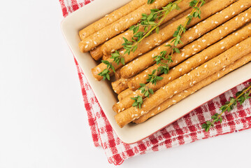 Baked homemade  bread sticks grissini with thyme stems and sesame. Dish with breadsticks on checkered table napkin