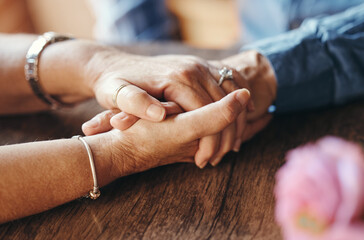 Macro, couple and elderly people holding hands on table for support, love and care in home. Zoom,...