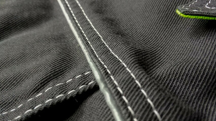 White stitching on black fabric. Texture black working clothes with white stitching closeup, green reflective elements