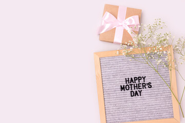 Happy Mothers day. Letter board, white gypsophila flower, gift tied with pink ribbon on a gray background. Festive concept with copyspace.