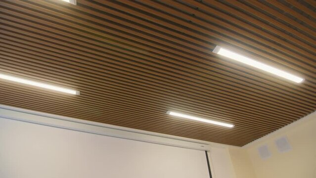 Glowing led lamps on ceiling decorated with wooden planks in office low angle shot. Light equipment installed in room