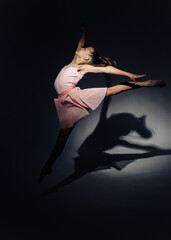 Ballerina child girl dances lit by light on dark background.