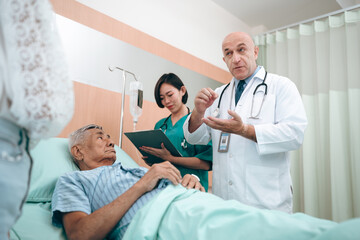 Obraz premium professional doctor standing by explain the treatment information via male elderly patient lying in bed in private hospital sickroom. The treatment program is suitable for people to socialize elderly