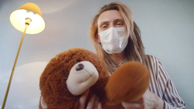 Low angle view of young father in safety mask hold teddy bear playing with baby. Realtime