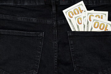 Stack of hundred dollar bills in back pocket of black jeans, denim background texture. Spending Money. Close-up.