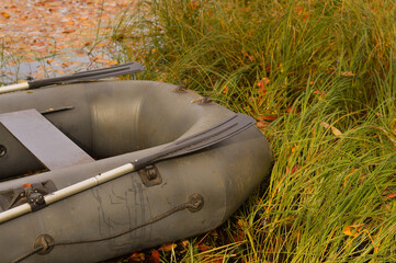 Close-up of an inflatable rubber boat standing on the shore of a swampy pond among autumn fallen leaves and grass, the concept of active recreation