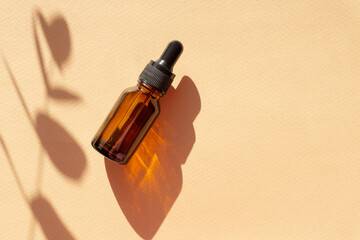 Essential oil in an amber-colored glass bottle with dropper lid next to shade of eucalyptus branch. Serum for care of women's skin on brown background. Flat lay, copyspace