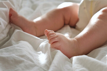 Obraz na płótnie Canvas Baby Legs Close up on White Blanket. Healthy Newborn Feet. Warm Sunlight. Beautiful Shot of Infant's Small Feet on a Light Background. Early age children development. Authentic Candid Lifestyle.