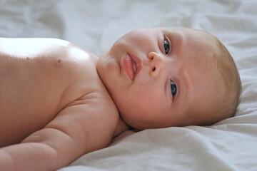 Closeup portrait of Newborn baby on white blanket. Soft focus. Infant is lying, yawning. One, two week age. Infant girl waking up on bed at home. New life and growing up concept. Real People.