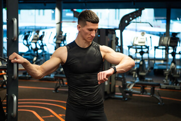 Fototapeta na wymiar Athlete checking up fitness tracker in gym. Athletic man monitoring fitness training in gym