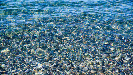Background of clear blue water and pebbles under crystal water, panoramic view