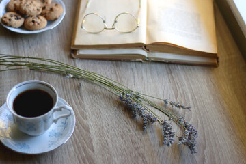 Cup of tea, plate with chocolate chip cookies, open book, reading glasses, lit candles and dry lavender flowers. Hygge at home, selective focus.