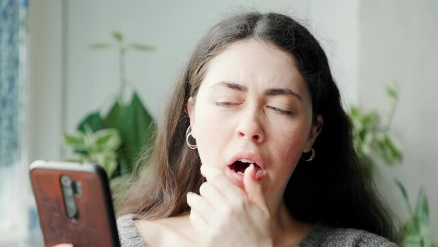 Portrait of boring and yawning woman bulging eyes using at a smartphone. Social media and boredom concept.