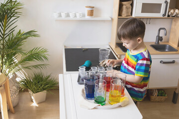 Cute baby boy learning mixing different colors with water and paint in containers. Early development
