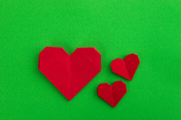 Red origami hearts on green background
