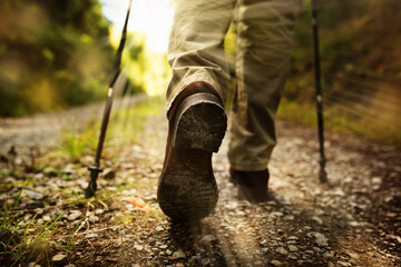 Hiker man with trekking sticks runs on a gravelled dirt trail in the terrain. Horizontal partial shot from behind with short depth of field and focus on boot. Space for text. - obrazy, fototapety, plakaty
