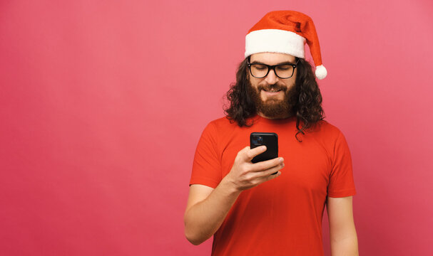 Long haired bearded man with Christmas hat looks at the phone he is holding.