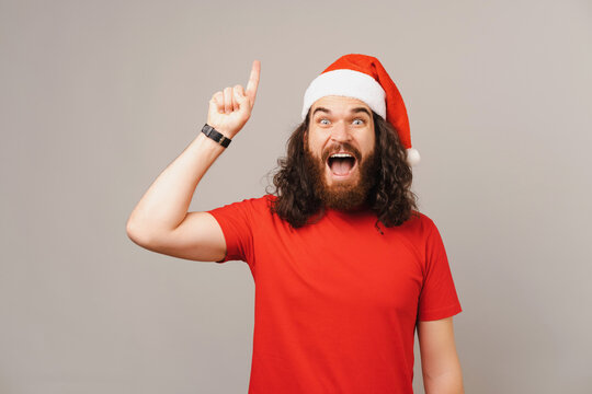 Excited bearded man with long hair points up while wearing a Christmas cap.
