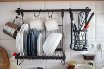 Clean dishes drying on metal dish rack on light background. Kitchen utensils and dishware. Kitchen interior background.
