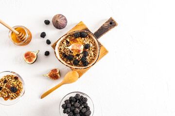 delicious healthy granola with dried fruits and honey, fresh blackberries and figs in a ceramic bowl on a cutting board. top view. white background.