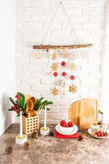a bouquet of spruce branches, burning candles, red balls and a handmade garland on a white brick wall in the interior of a modern kitchen .