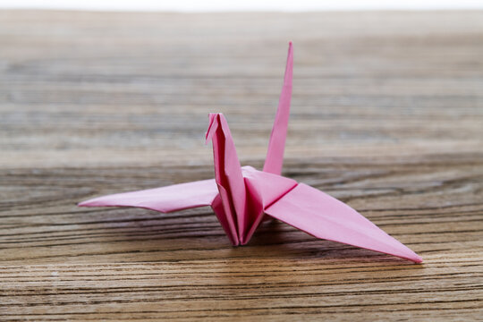 Pink origami paper crane on wooden table