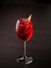 Red transparent cocktail with orange in a glass on a dark background