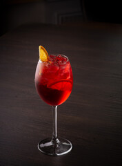 Red transparent cocktail with orange in a glass on a dark background
