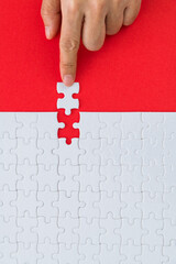 Hand putting the last piece of white jigsaw puzzle