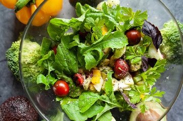 Glass bowl with fresh salad, greens, avocado and vegetables. Healthy food concept. Rustic style, top view