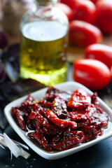 Sun-dried tomatoes in a bowl surrounded by ingredients, spices , garlic and basil to prepare. Rustic style
