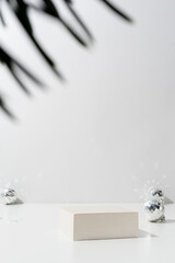 A minimalistic scene of a podium with christmas decorative balls and pine tree on light background