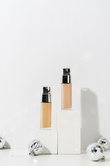 A minimalistic scene of foundation cosmetic bottle on podium with christmas decorative balls and pine tree on light blue background