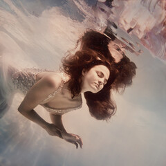 A girl with long dark hair in a white dress poses underwater like a bkdto in zero gravity