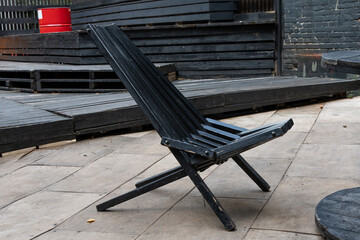A wooden black folding chaise longue stands outside on the street